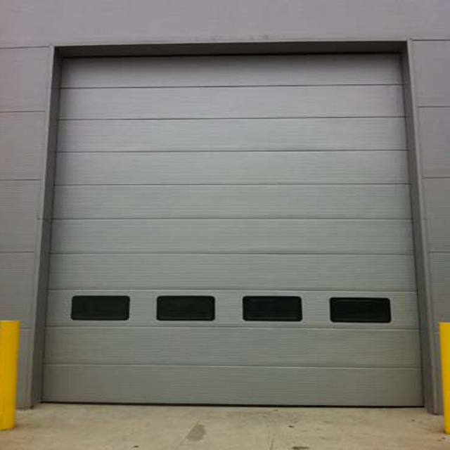 Puerta industrial seccional estilo micrograno color gris plateado con ventanas 